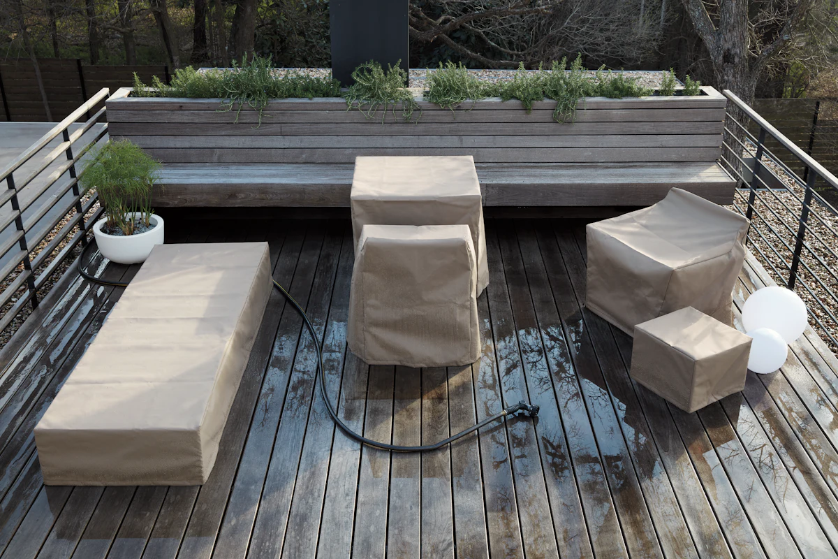 Outdoor seating arrangement with beige protective covers: long bench, a central cube, two square stools, a small cube, and a white balloon-like decoration on a wooden deck.