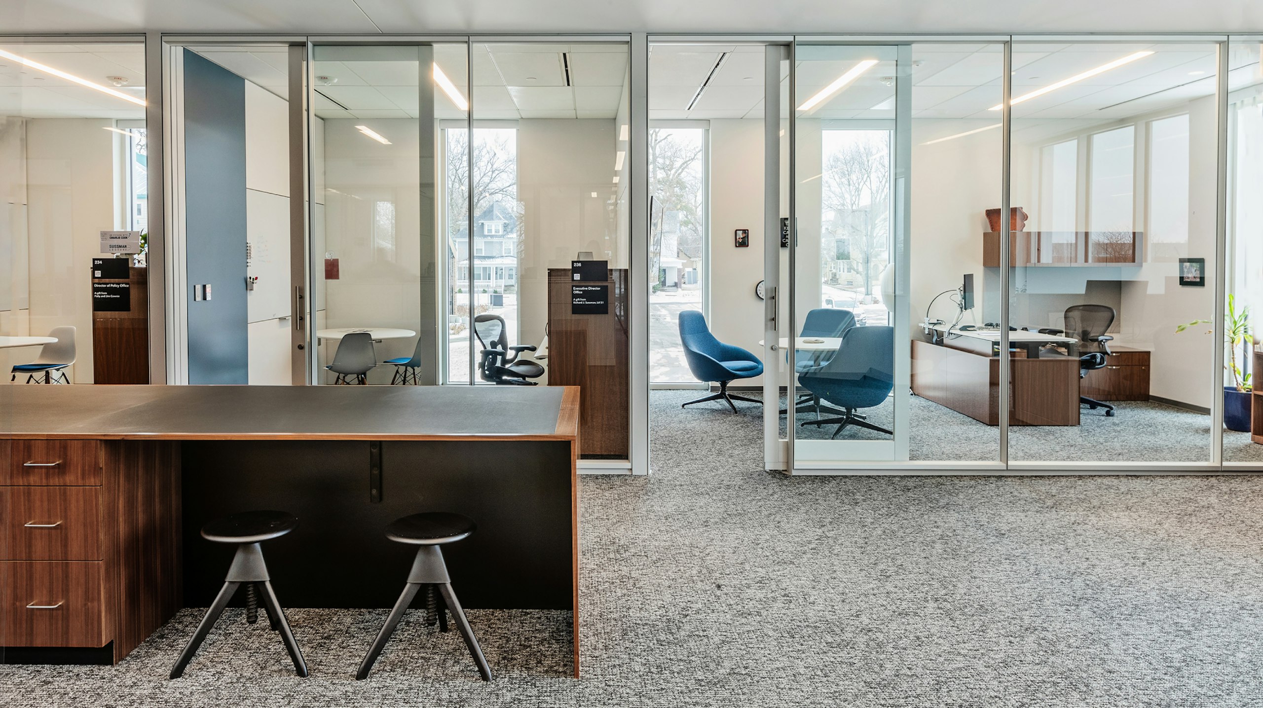 Open workspace in an academic research institute with a storage island and two stools with private offices behind.