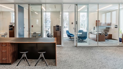 Open workspace in an academic research institute with a storage island and two stools with private offices behind.