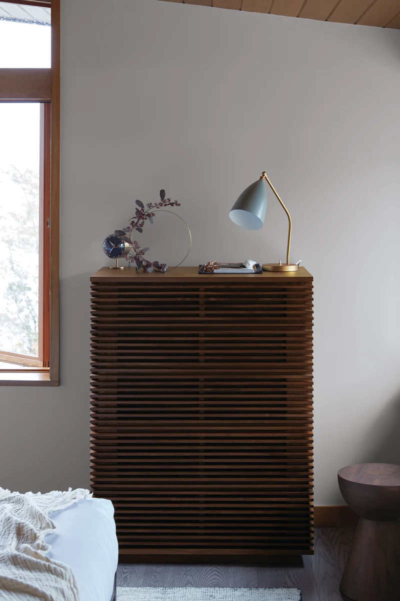 Tall wooden slatted cabinet with desk lamp and decorative items on top