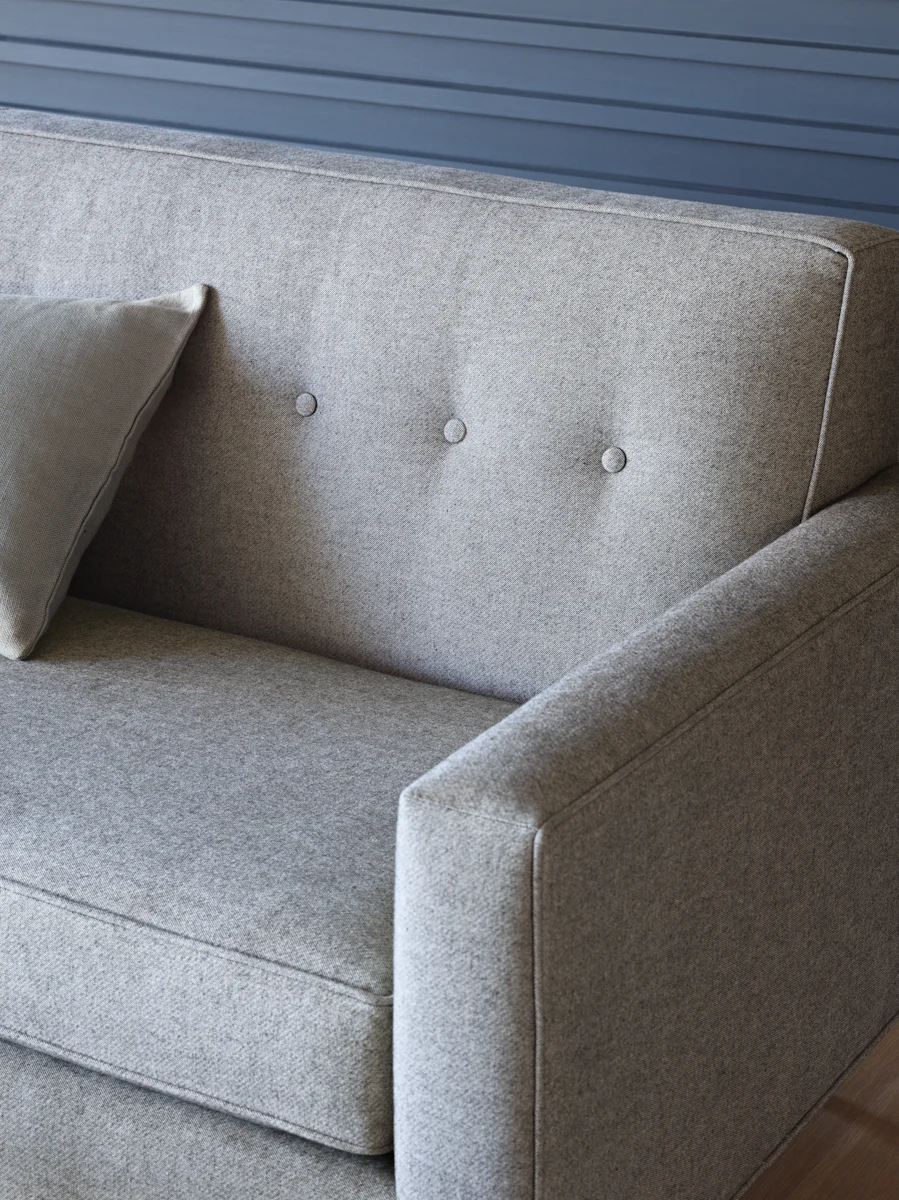 Close-up of gray fabric sofa back cushion with button tufting and seam stitching.