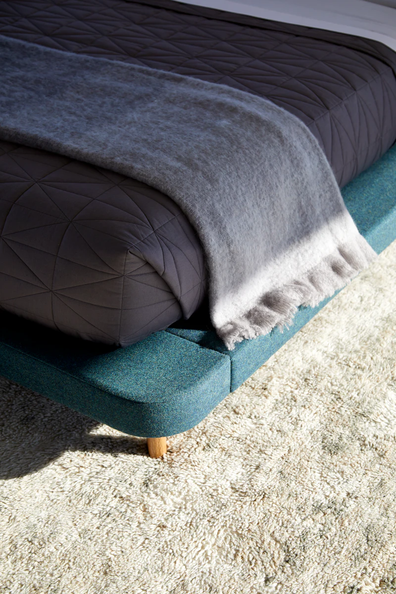 Low-profile teal bed with dark quilt and folded blanket, showing bed frame corner.