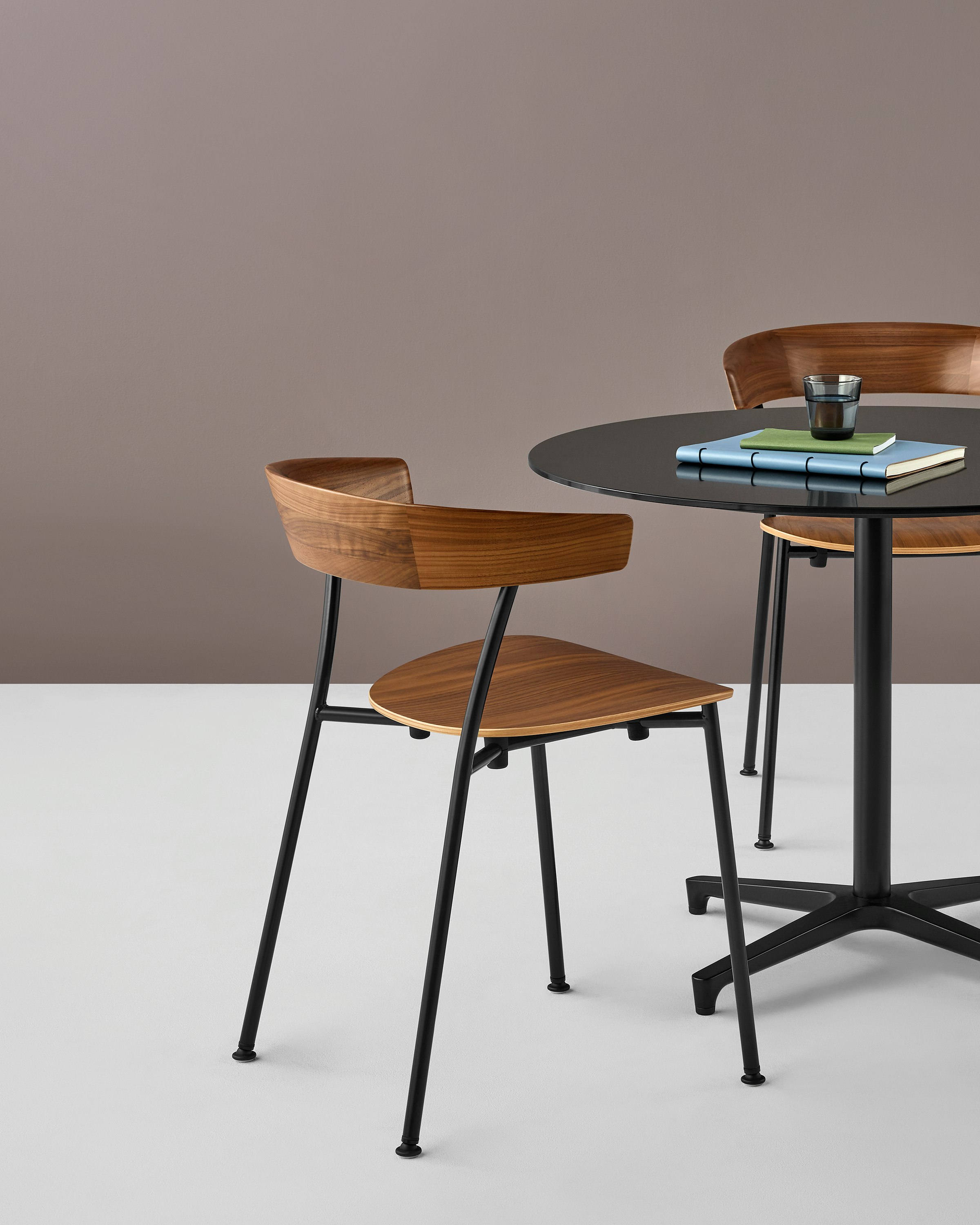 A stackable Leeway Chair with a metal frame and wood seat and backrest next to a black table with a round top.
