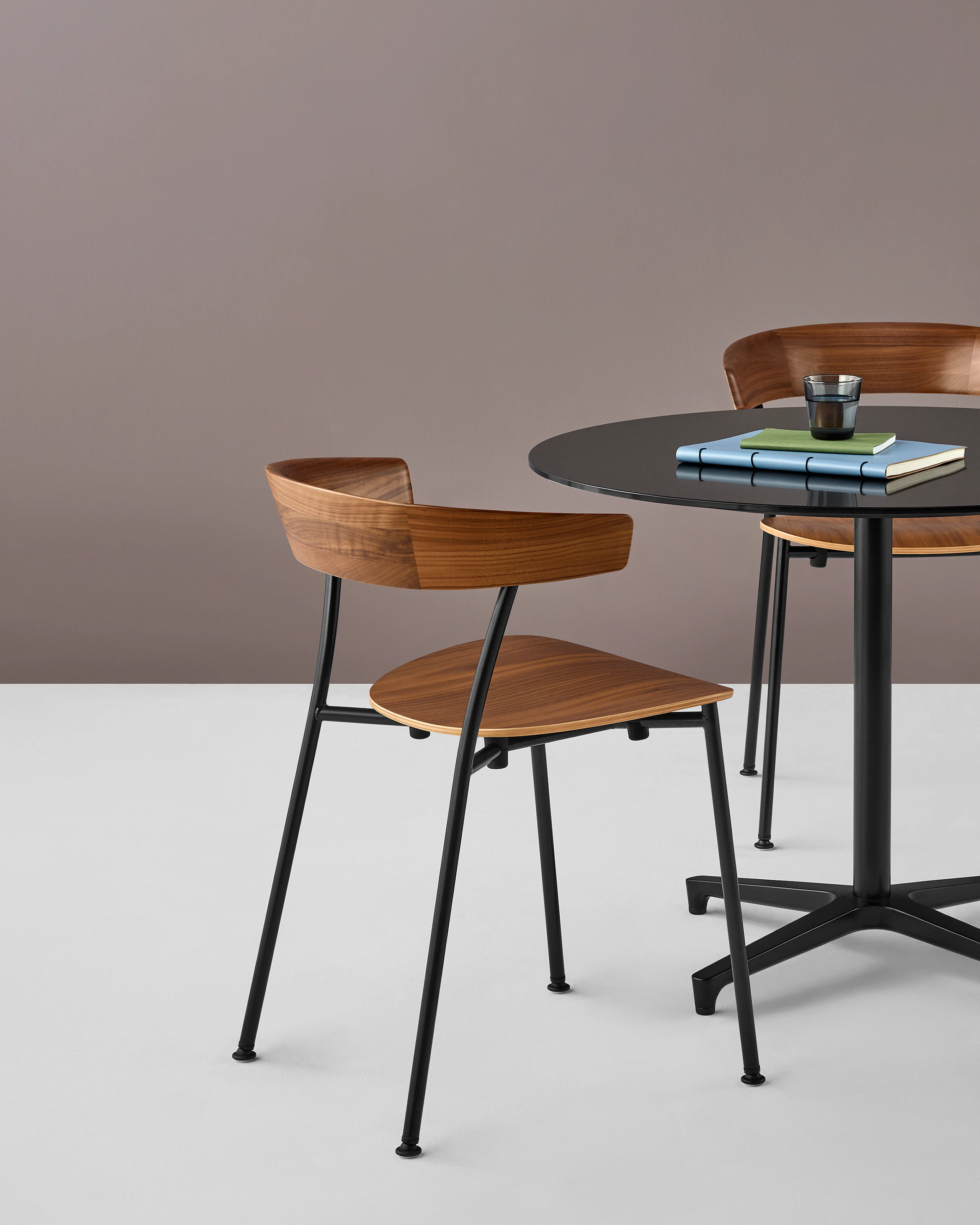 A stackable Leeway Chair with a metal frame and wood seat and backrest next to a black table with a round top.