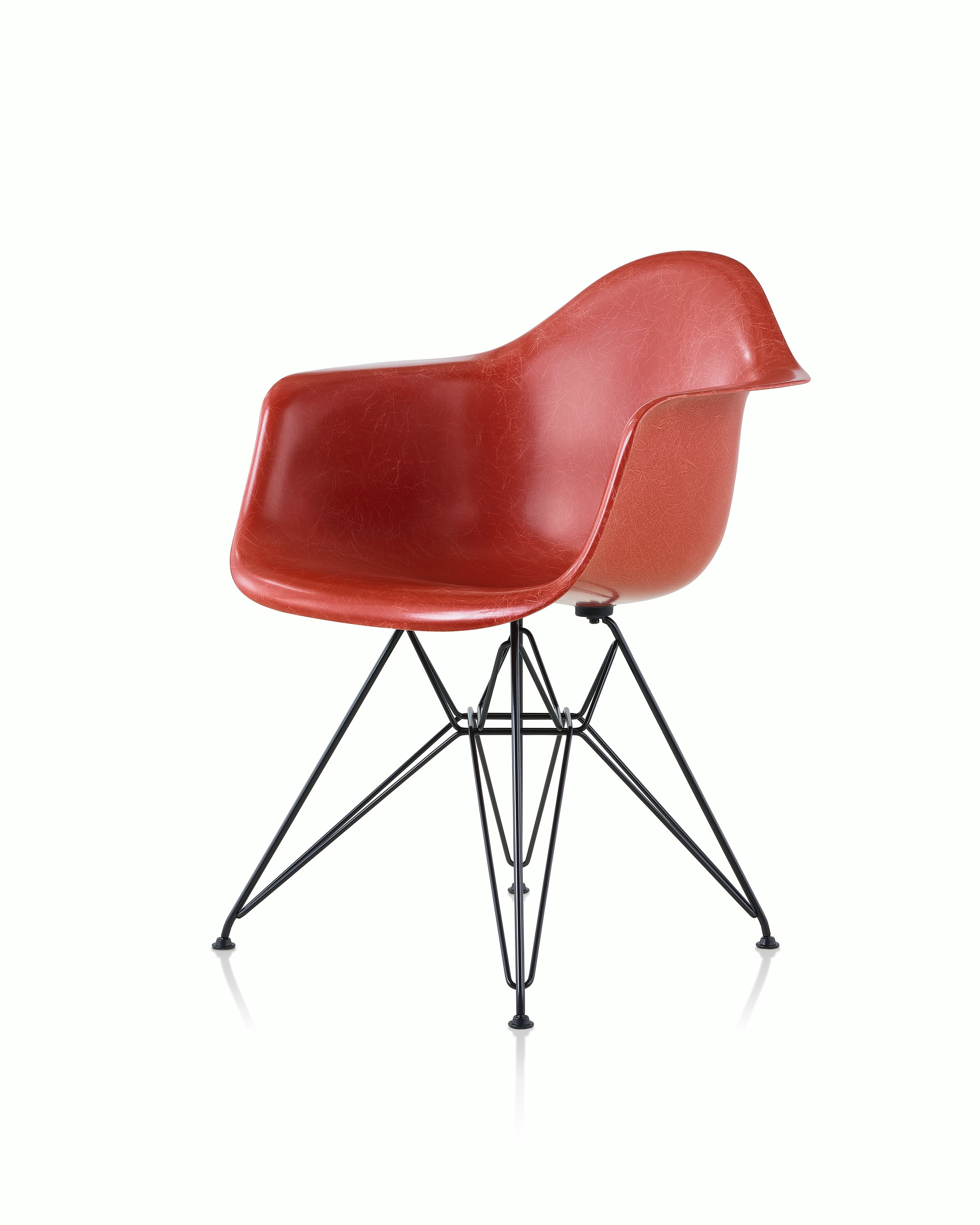 A red Eames Molded Fiberglass Chair with arms and a wire base, viewed at an angle.