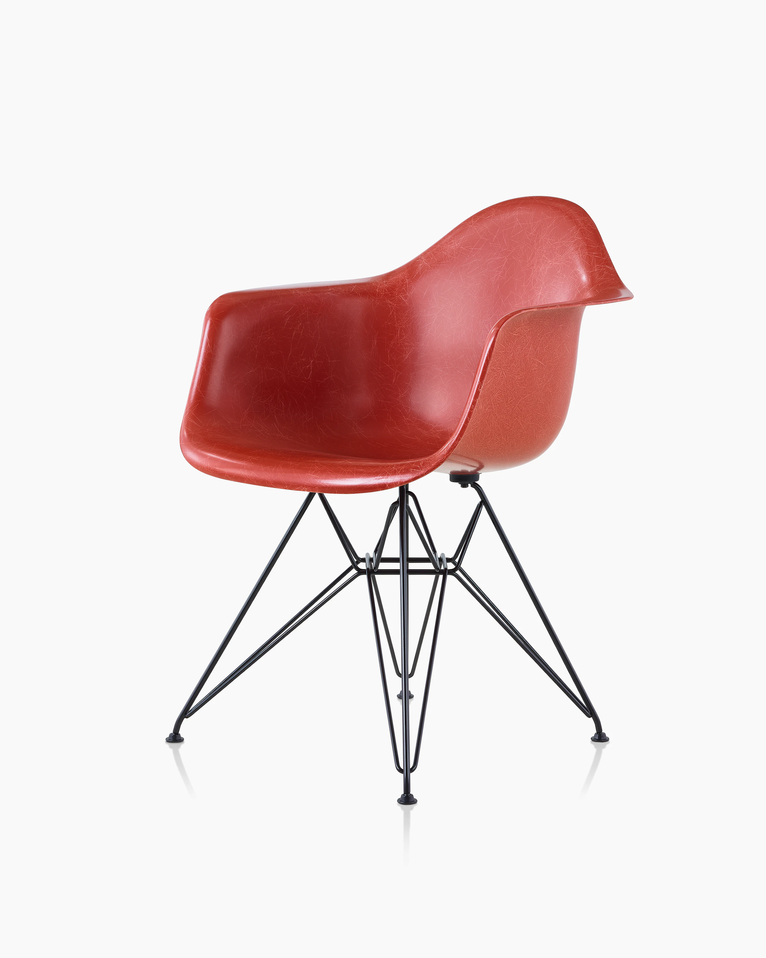 A red Eames Molded Fiberglass Chair with arms and a wire base, viewed at an angle.