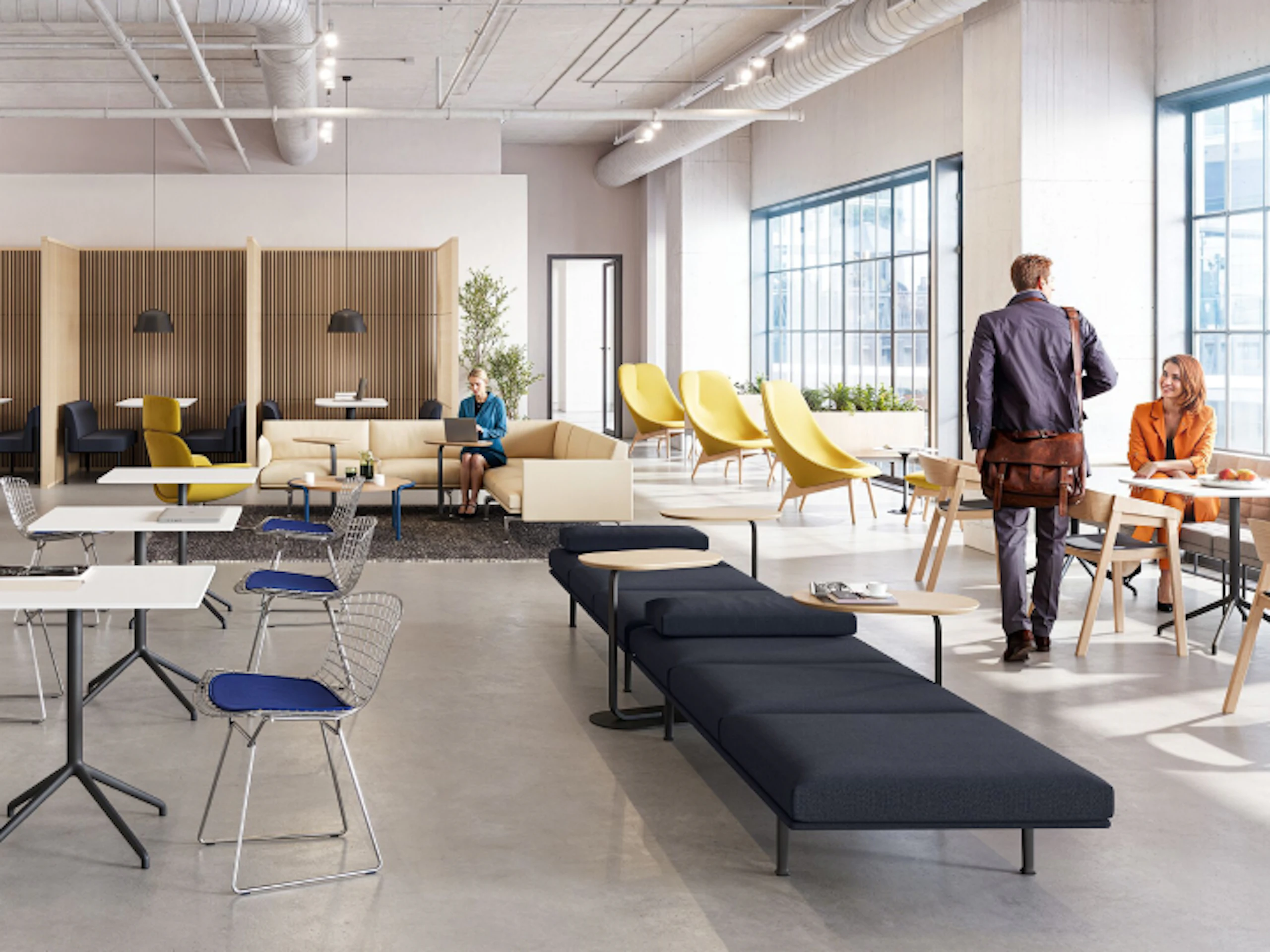 A brightly lit community space featuring three people utilising a variety of colourful seating options including the HAY Uchiwa Lounge Chair, Muuto Base Tables and Muuto Still Cafe Tables