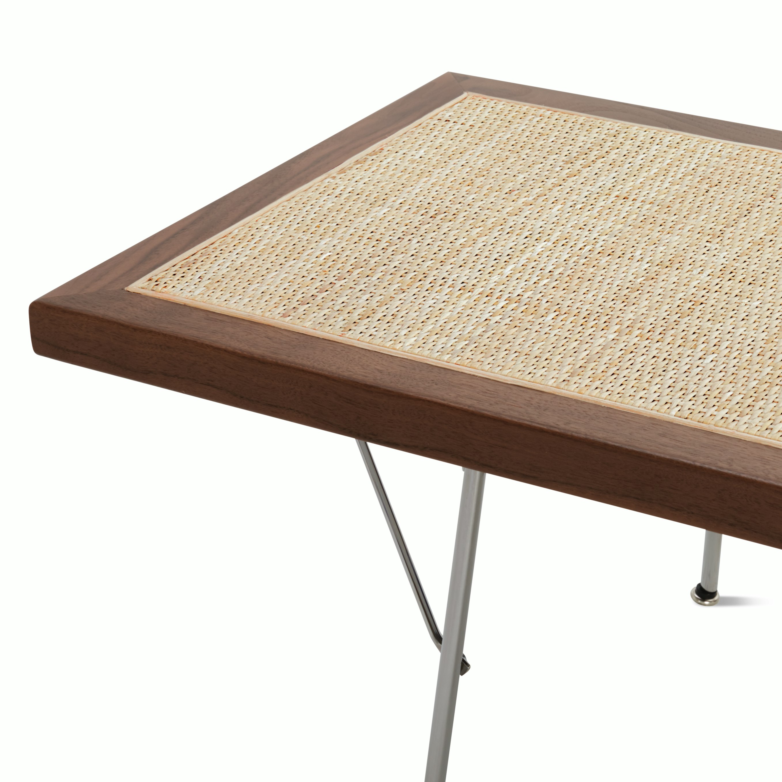 A close up detail of the walnut frame, cane detailing, and metal legs of the Nelson Cane Bench.