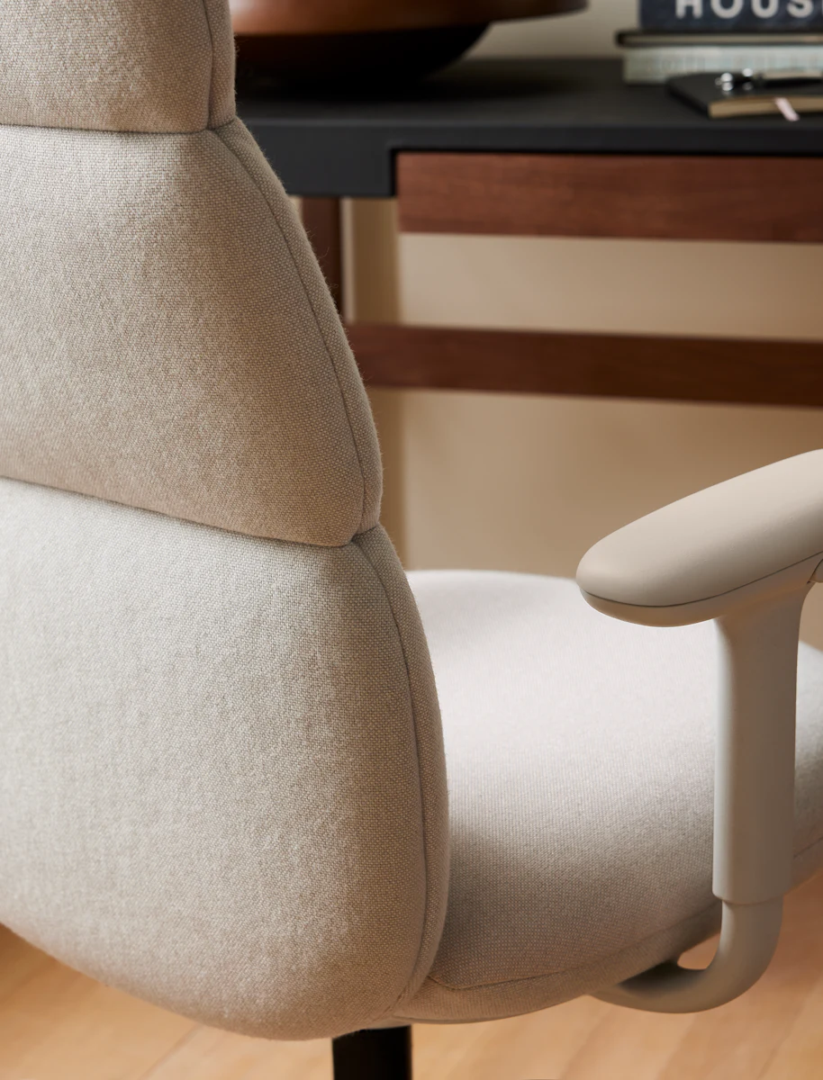 Close-up of a beige upholstered office chair armrests and back with a desk behind