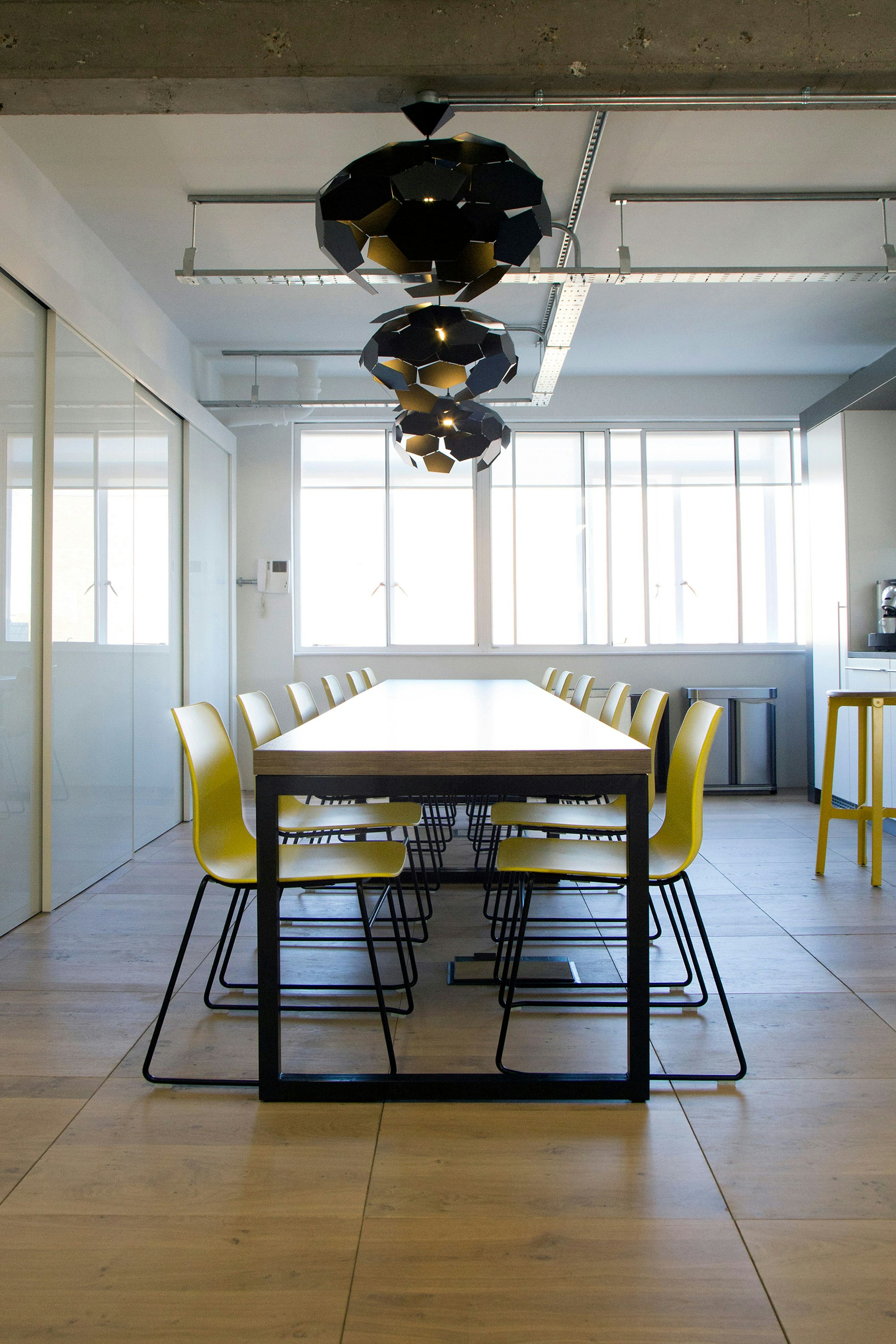A view down a long conference table with twelve yellow Polly Side Chairs with black sled bases pushed underneath.