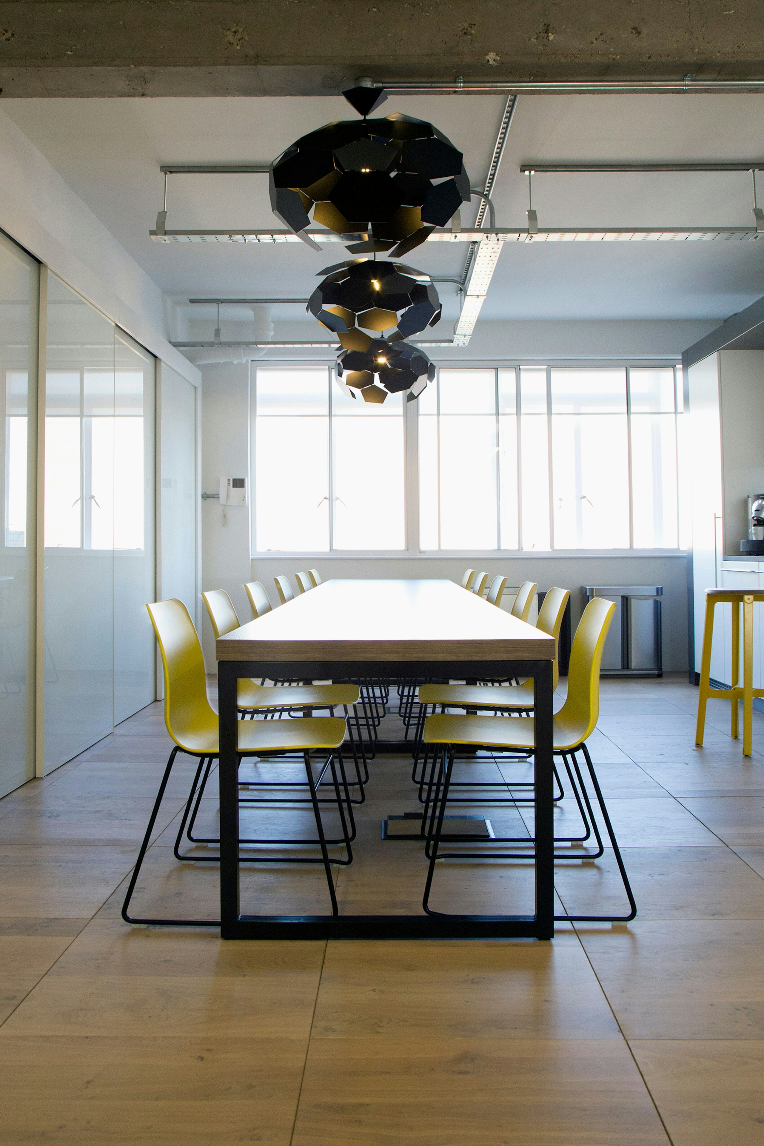 A view down a long conference table with twelve yellow Polly Side Chairs with black sled bases pushed underneath.