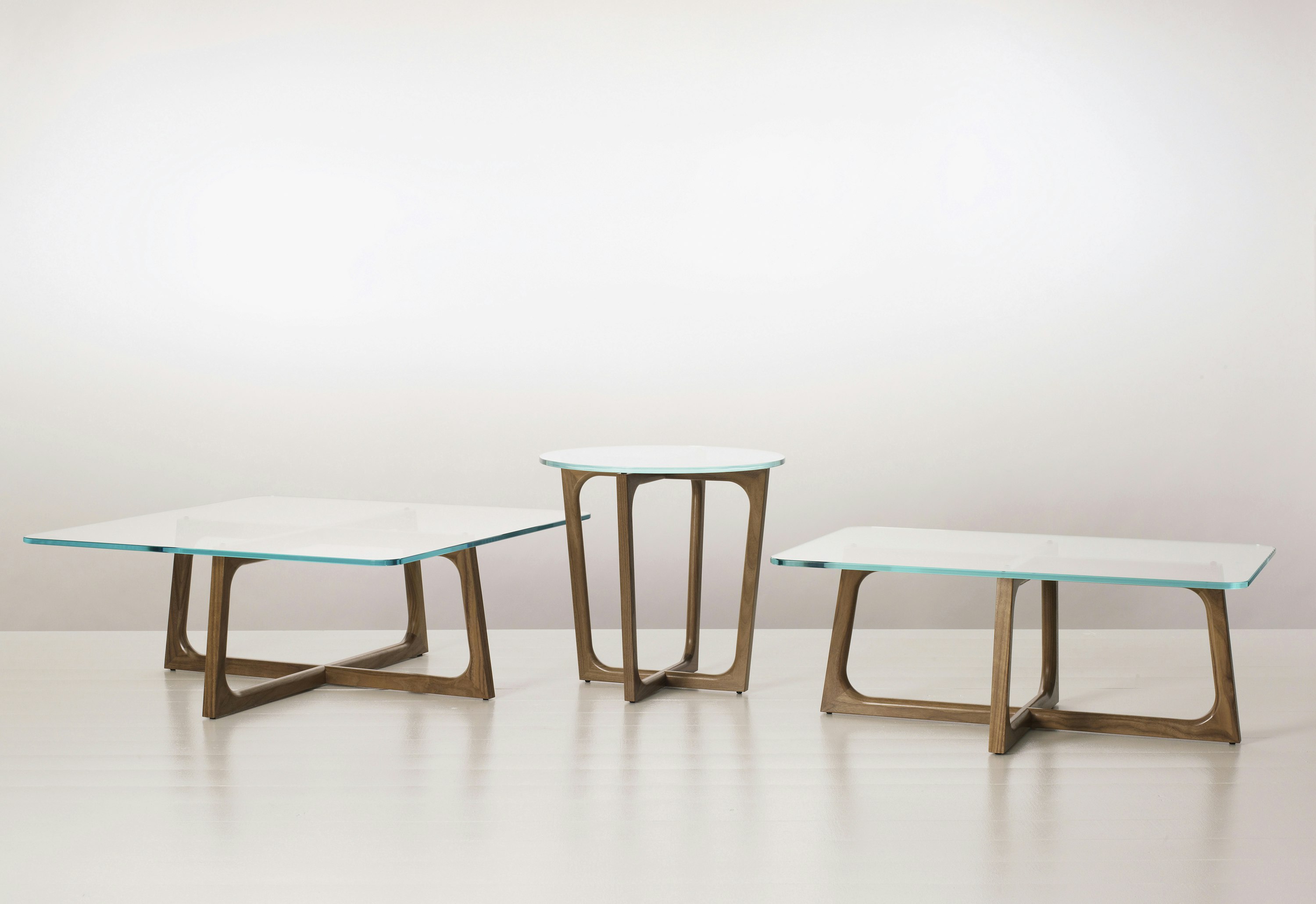 Three Loophole occasional tables of different sizes and shapes, each with a glass top and walnut base.
