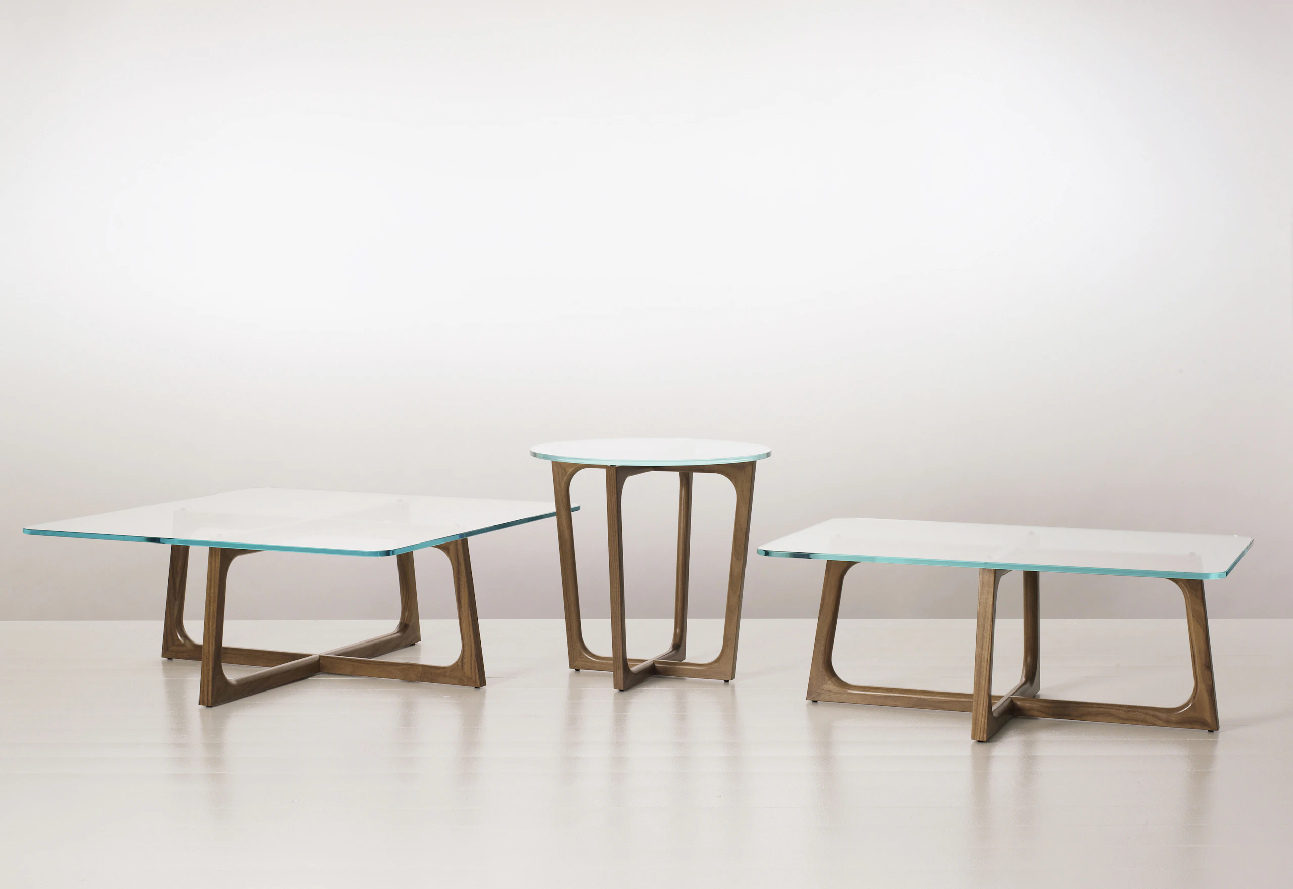 Three Loophole occasional tables of different sizes and shapes, each with a glass top and walnut base.