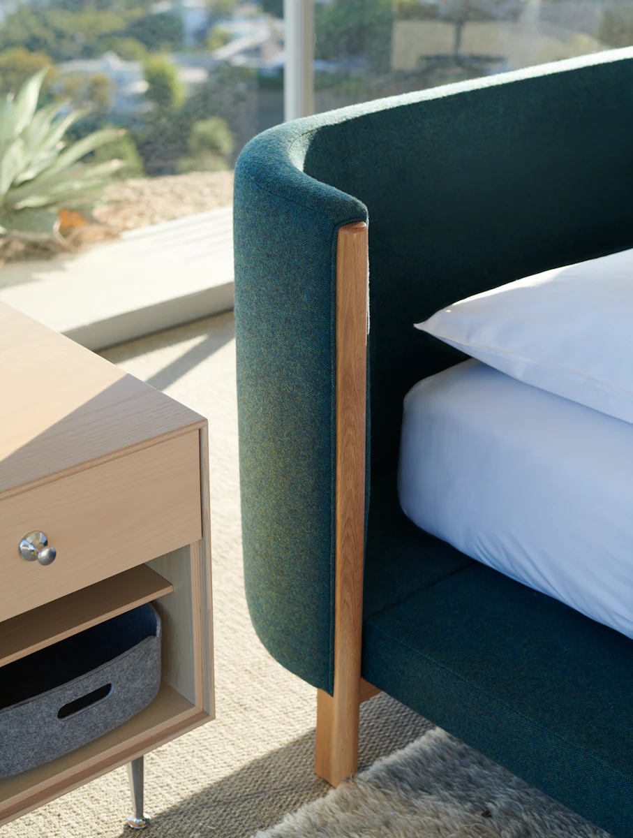Modern bedroom with teal bed, large windows, and minimalist seating.