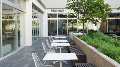 Several white Eames Wire Chairs by Herman Miller arranged at tables next to green foliage outside the MillerKnoll Dallas showroom
