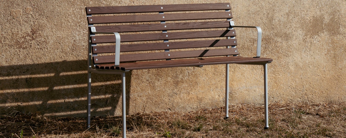Traverse Dining Bench with Arms against an outdoor stucco wall
