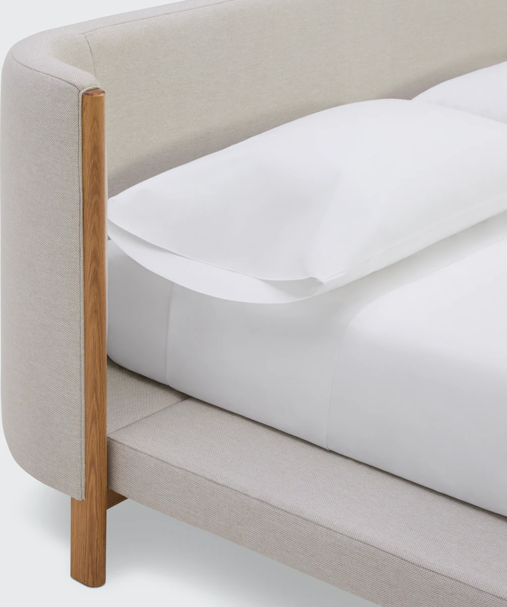 Back view of an upholstered headboard with light fabric and wooden feet.