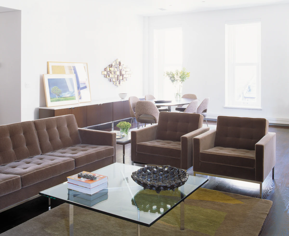 Living room with glass coffee table and two chairs facing a sofa, greenery outside