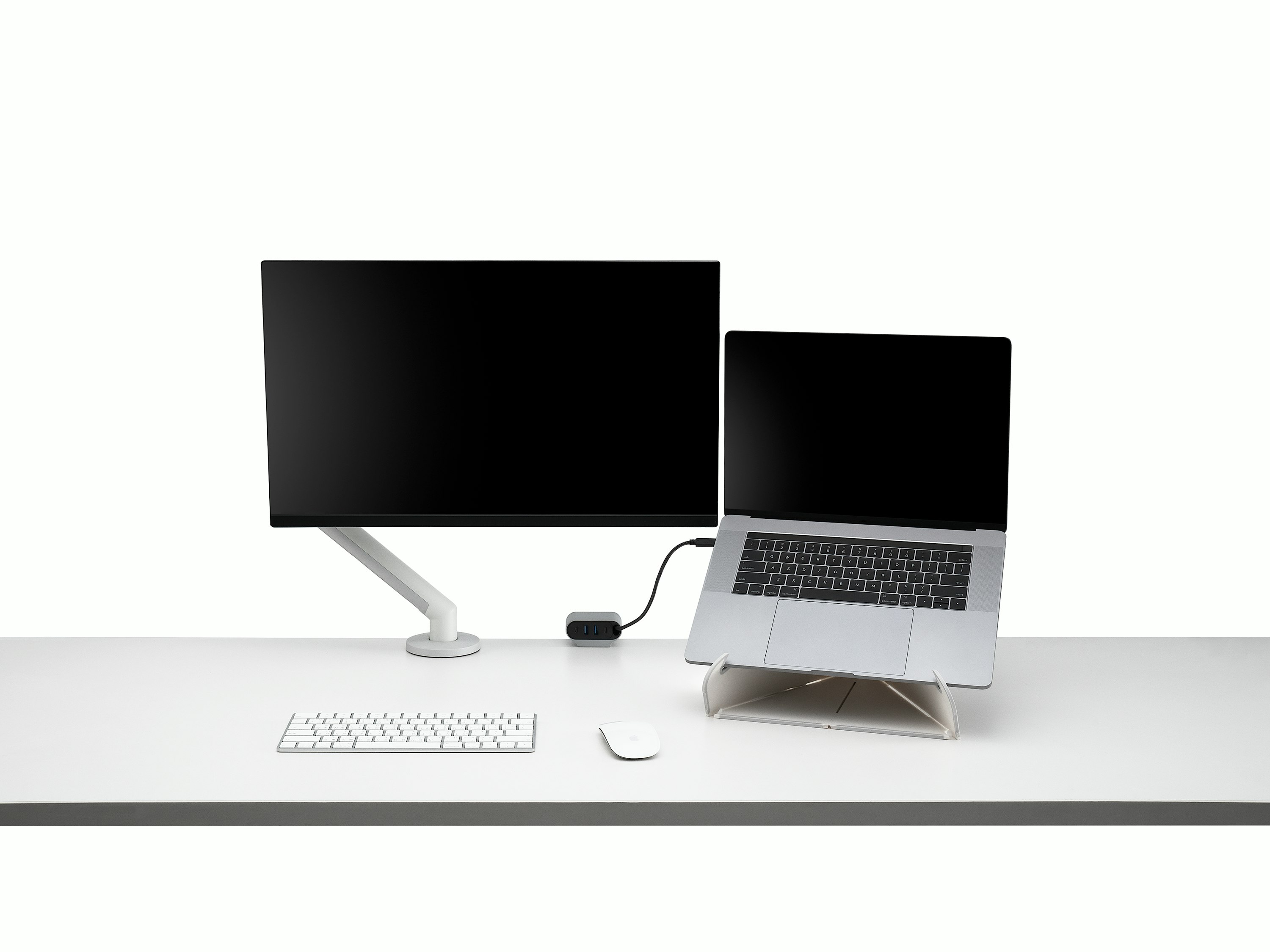 Front view of a screen attached to a Flo Monitor Arm integrated with an Ondo Work Surface Mount on a desk connected to a laptop with wireless keyboard and mouse that's supported by an Oripura laptop stand.