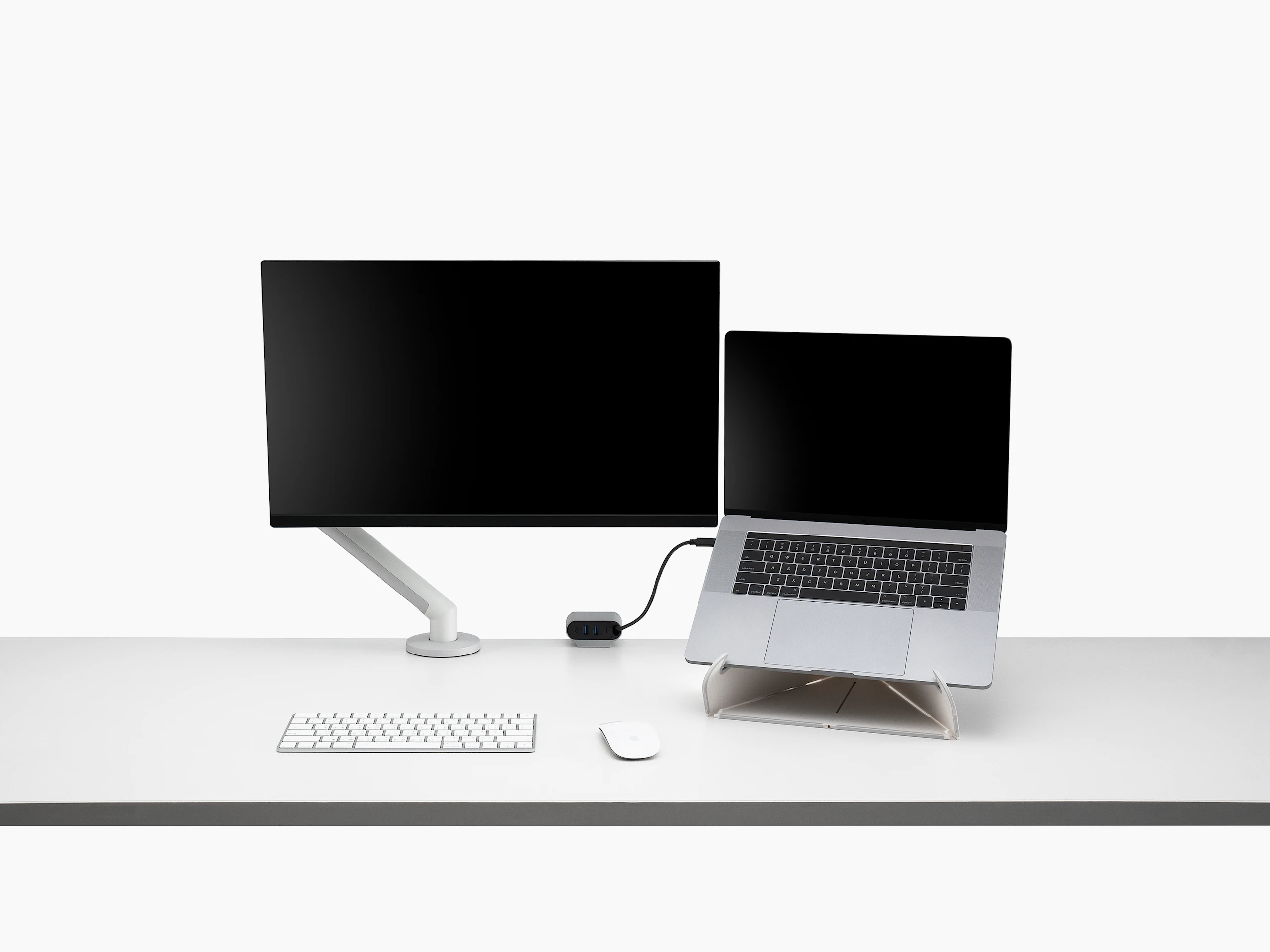 Front view of a screen attached to a Flo Monitor Arm integrated with an Ondo Work Surface Mount on a desk connected to a laptop with wireless keyboard and mouse that's supported by an Oripura laptop stand.