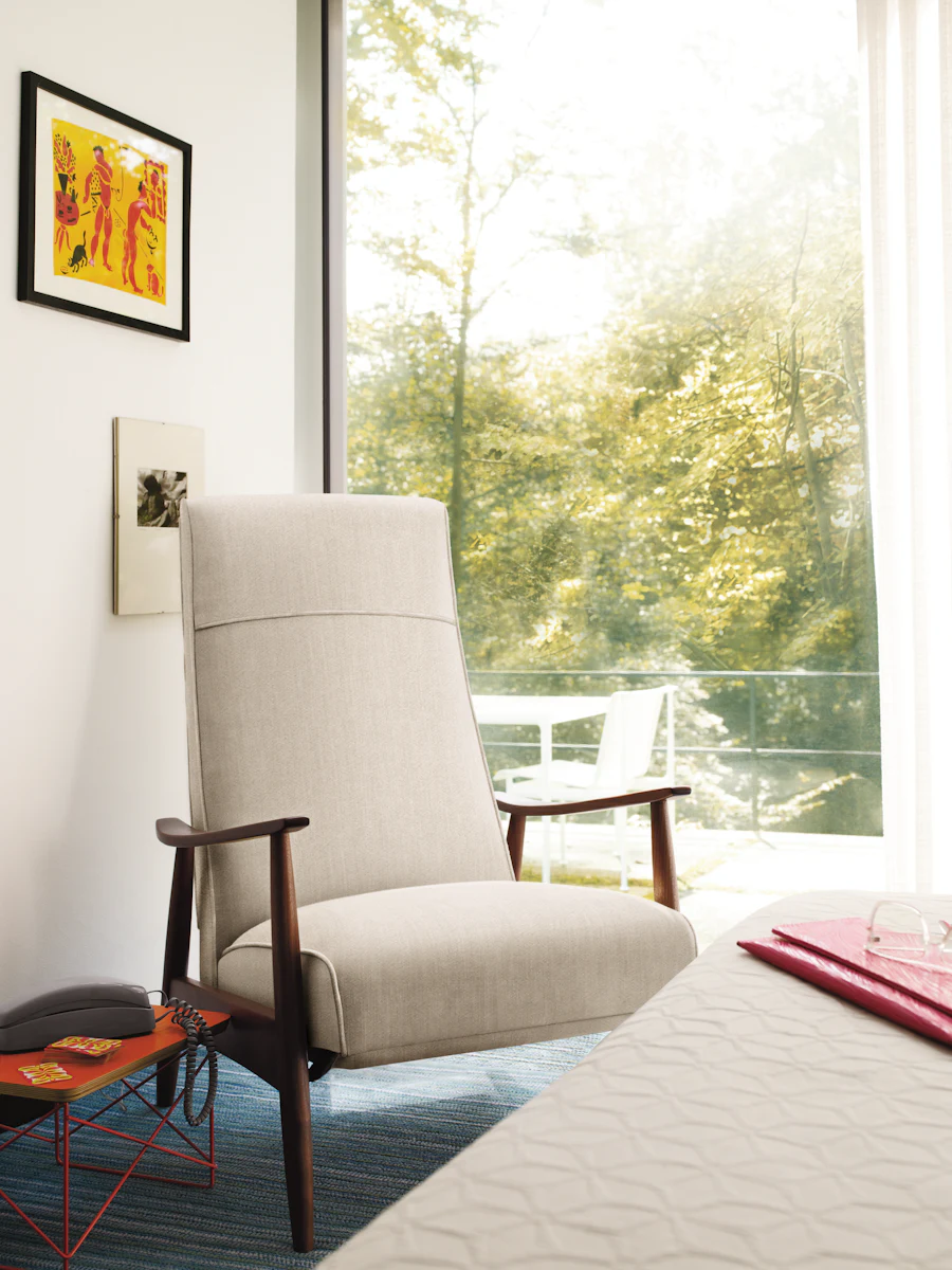 Beige upholstered lounge chair with wooden legs and armrests placed in a contemporary room near a window.